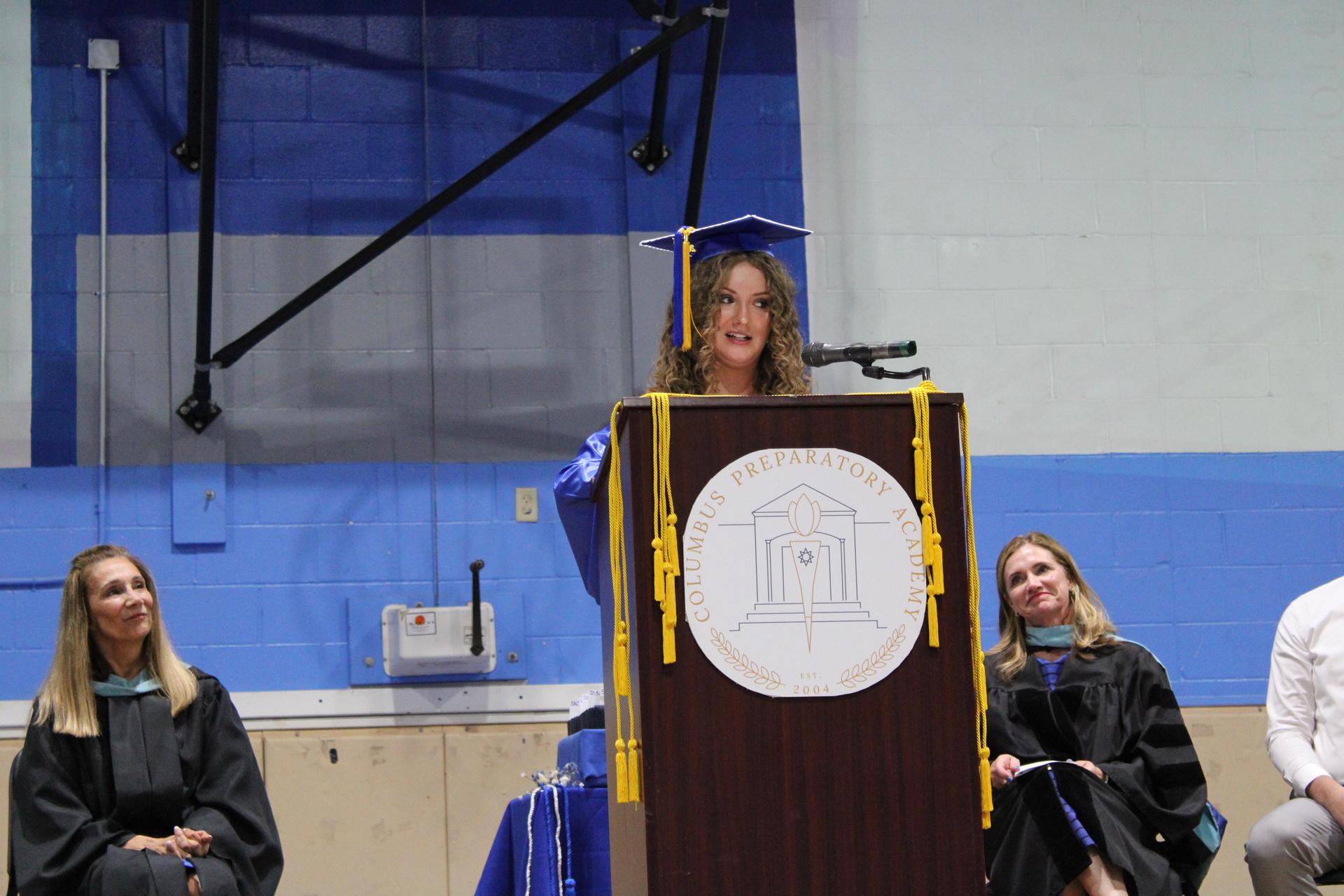 Graduate standing at a podium in cap and gown.