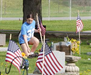 A student places an American flag on the gravesites of veterans.