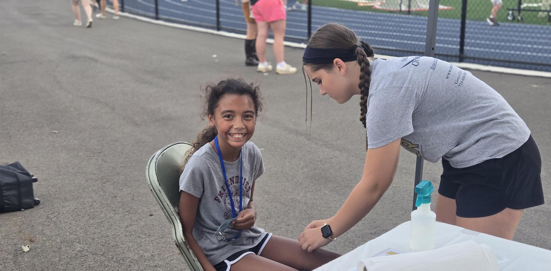 Girl smiling while receiving care on a chair at a sports track event.