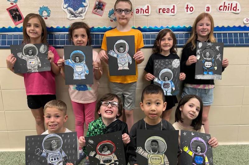 Students hold up a self-portrait they created with astronaut theme