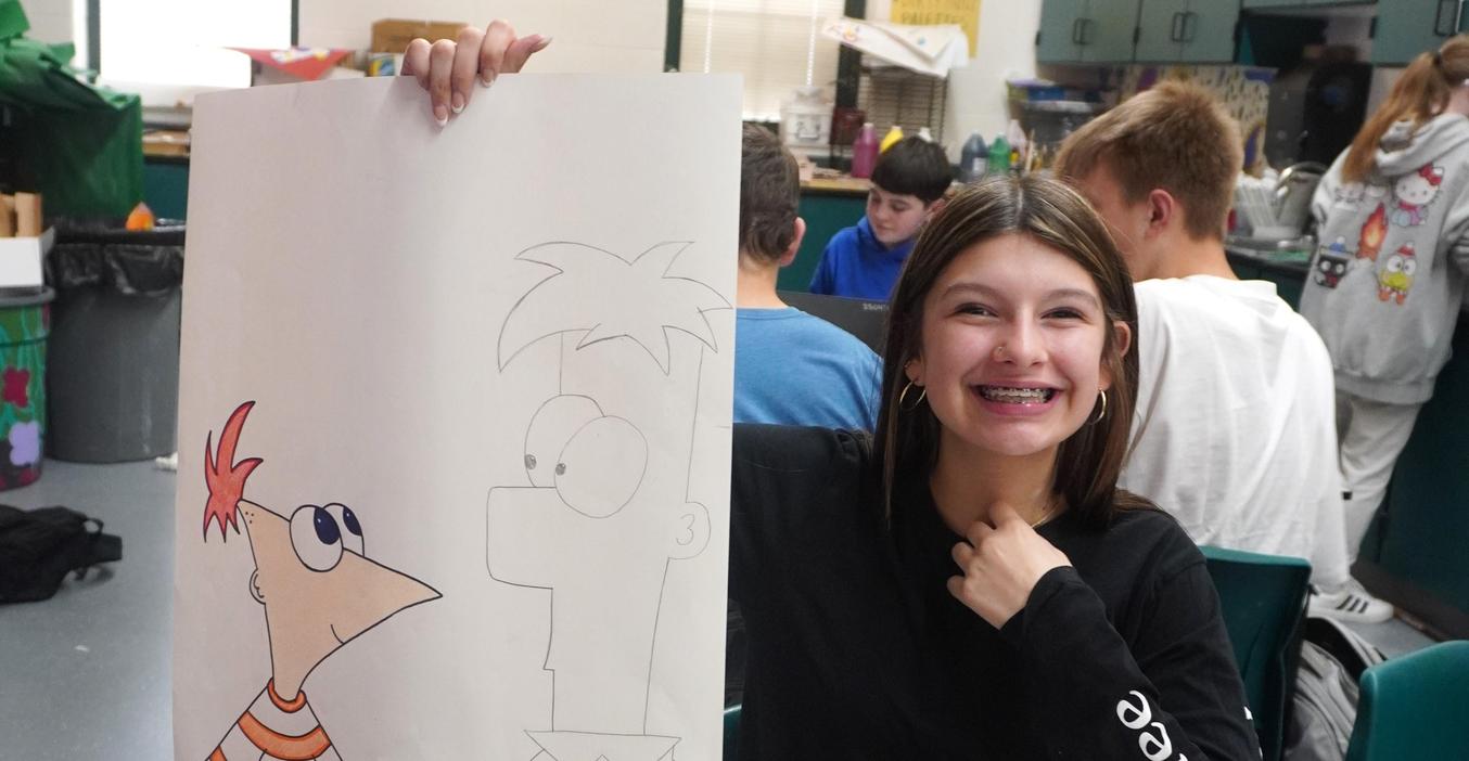 A middle school student holds up the drawing she is making of "Phineas and Ferb."