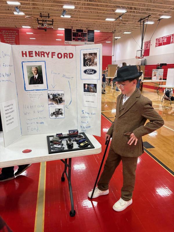 Boy in a brown suit and hat showcasing a project on Henry Ford.