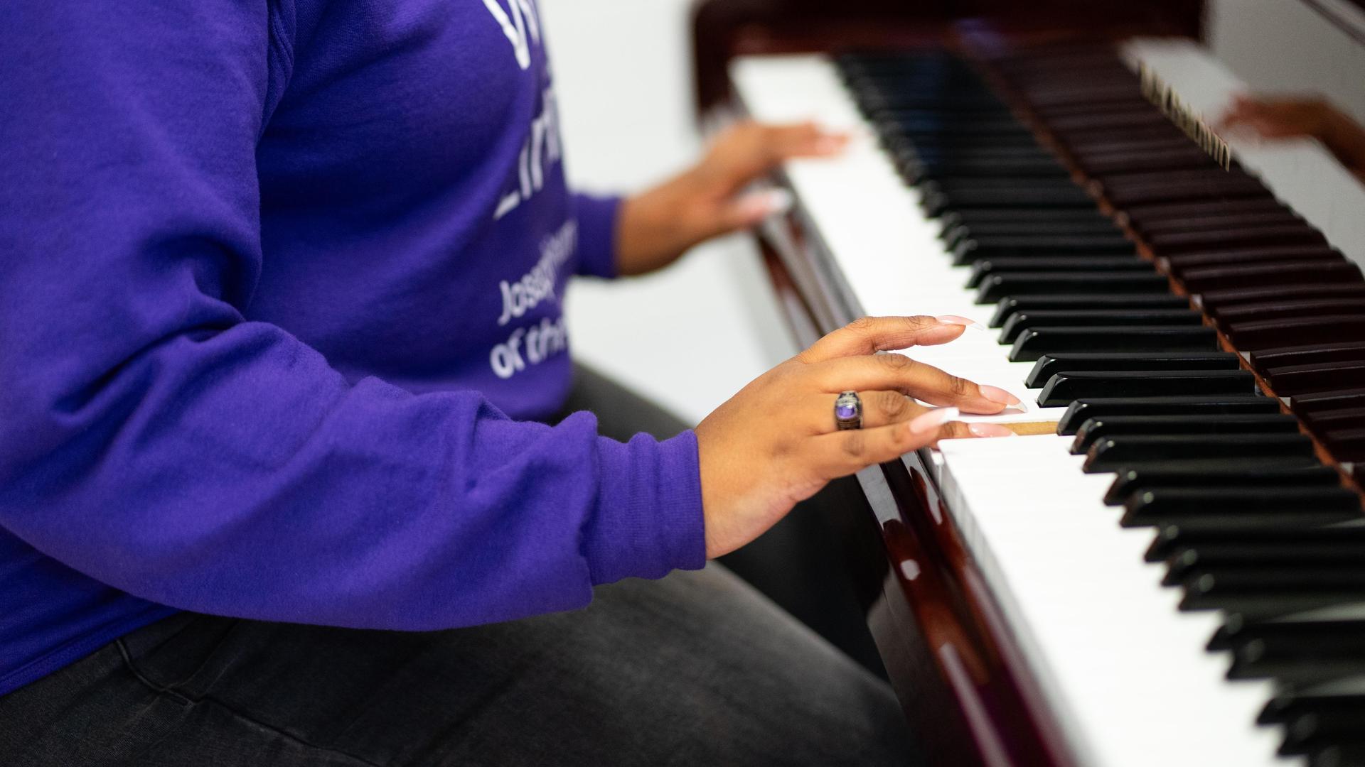 A person wearing a purple hoodie playing piano keys with one hand.