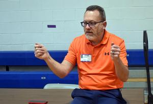 Man in an orange shirt gesturing during a discussion at a table.