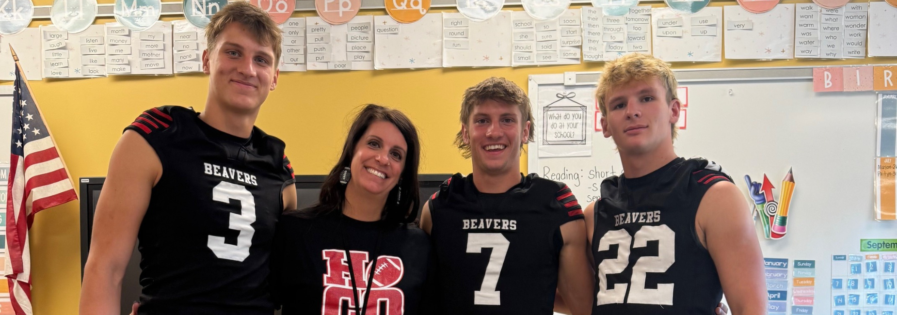 Four football players with a teacher in a classroom setting.
