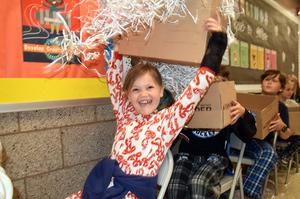 Child in festive pajamas joyfully holding up a box with shredded paper.
