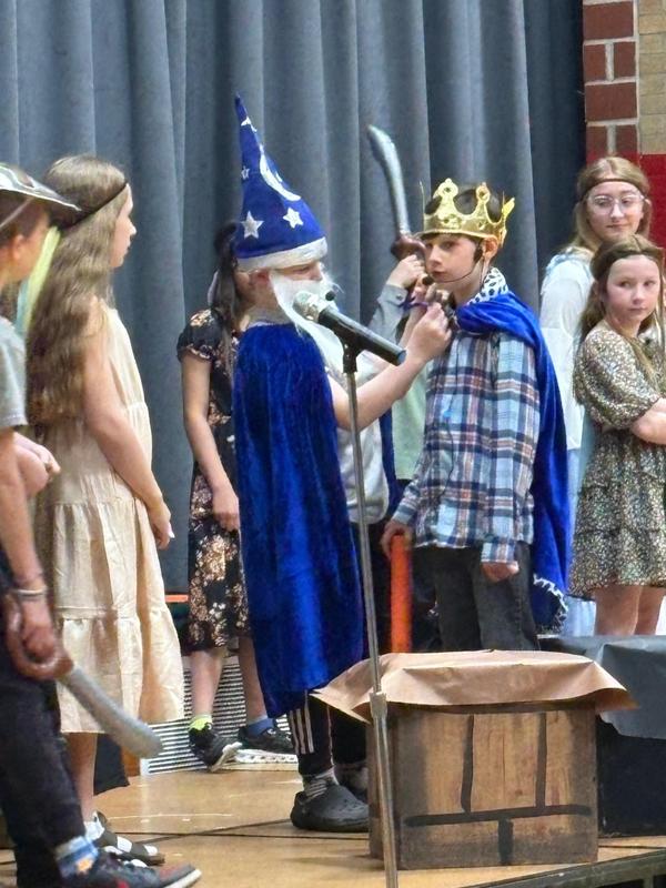 Child in a wizard costume participates in a scene on stage.