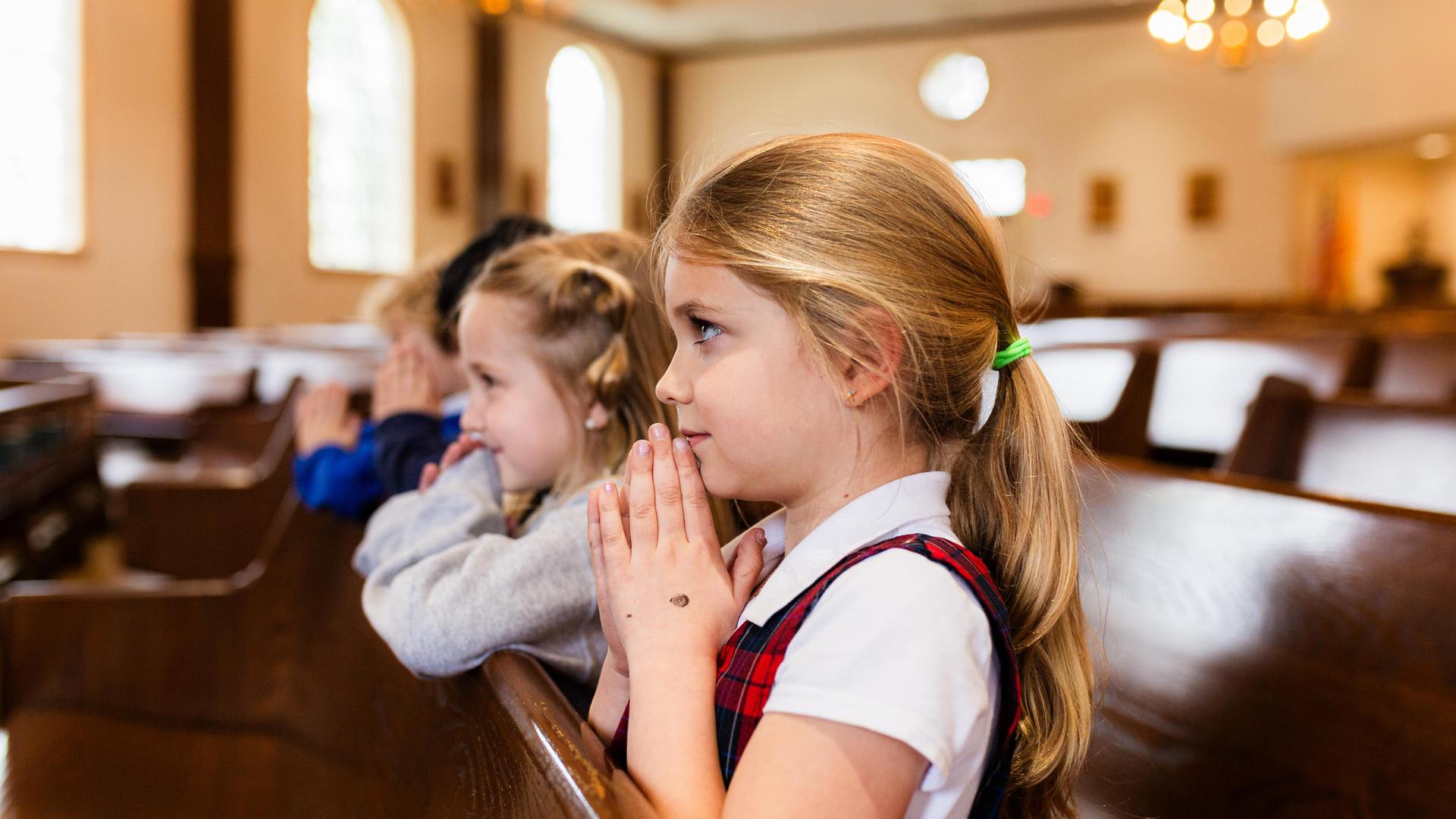 Children with clasped hands, praying in a church pew.