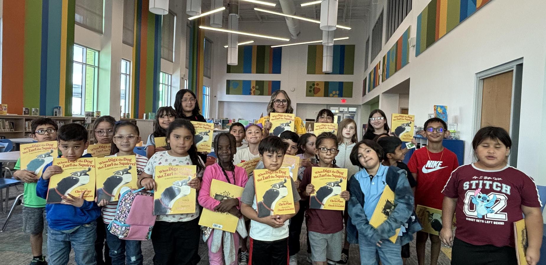A group of children and adults holding books in a colorful library setting.