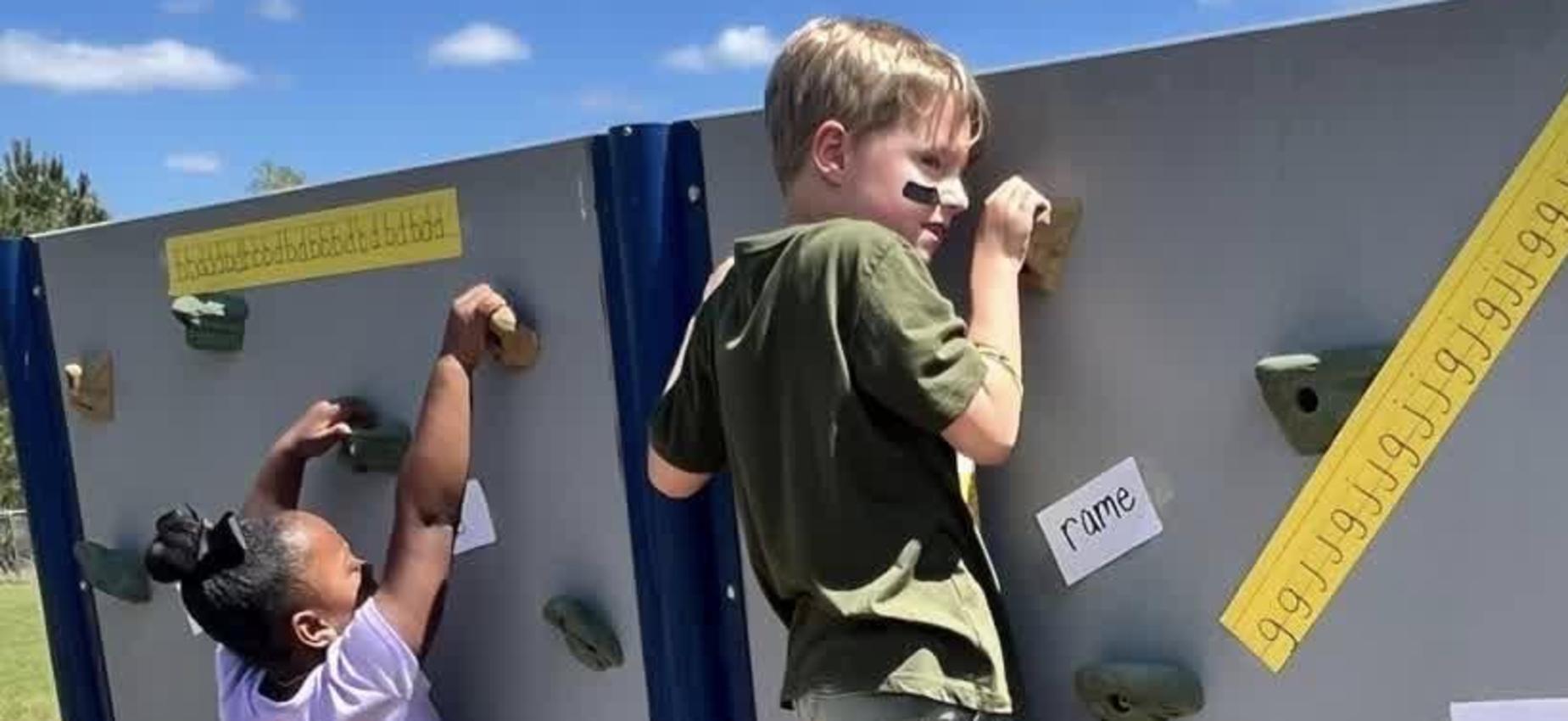 Kids climbing a rock wall with labeled holds for guidance.