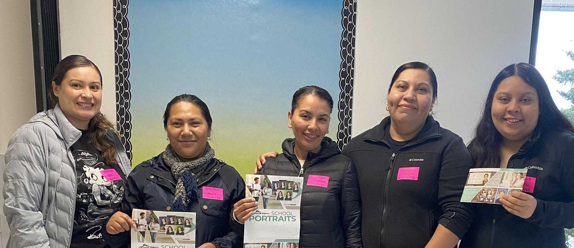 Five individuals in jackets, holding school portrait brochures, smiling for the camera.