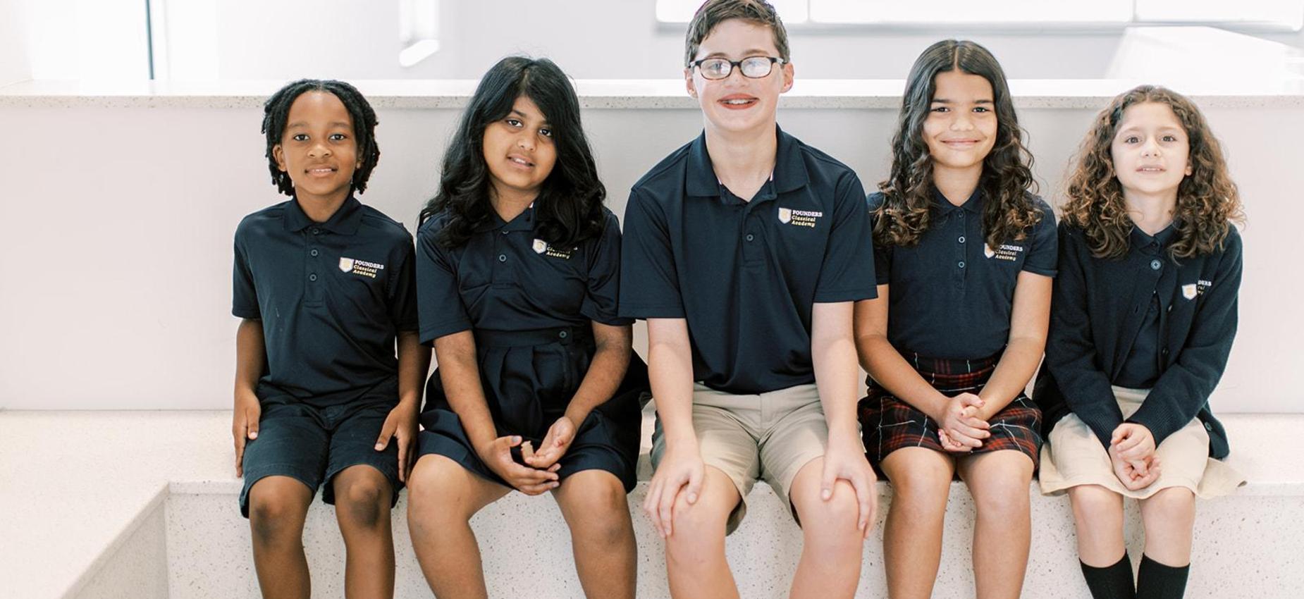 Five students in navy Founders uniforms sitting together and smiling