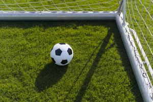 A soccer ball rests on the grass near the corner of a goalpost.