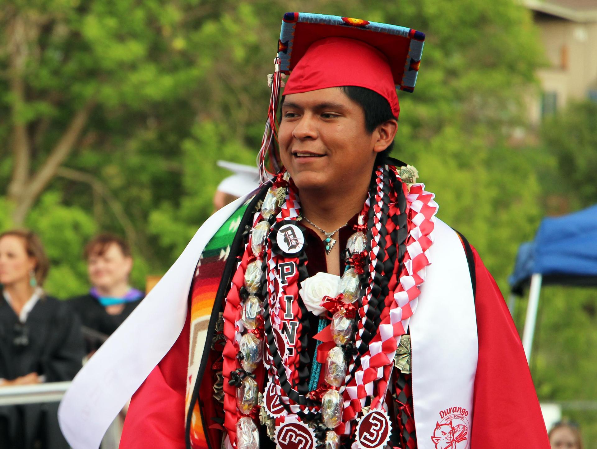 Native American student wearing graduation cap and gown looks off to the side