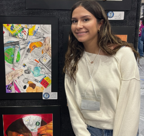 Student stands next to artwork collage depicting every day objects like color pencils, a ballet slipper, and Rubik's cube