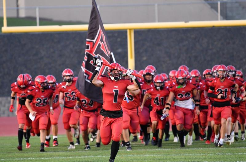 Picture of EVHS varsity football storming the field with center player holding and East Valley flag.
