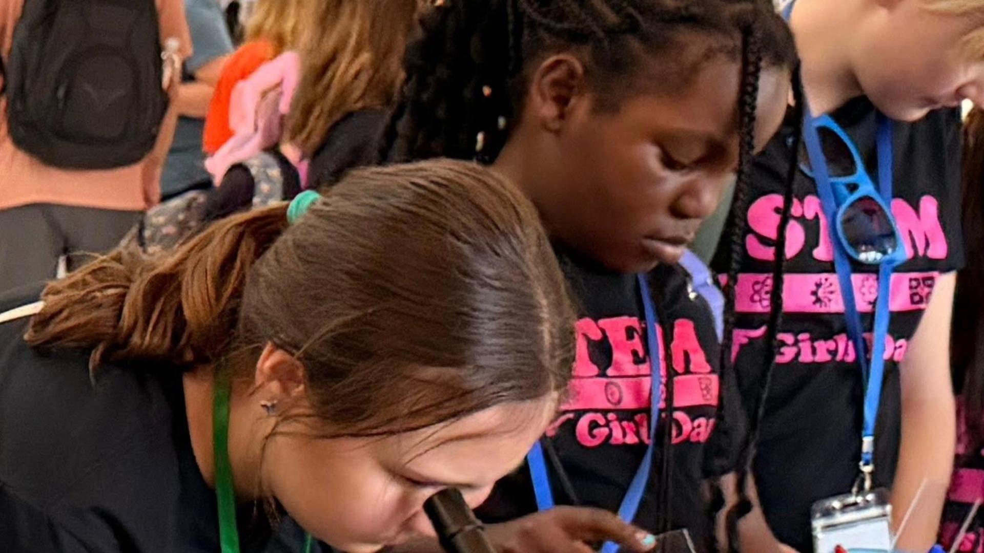 Two children examining objects through microscopes at a STEM event.