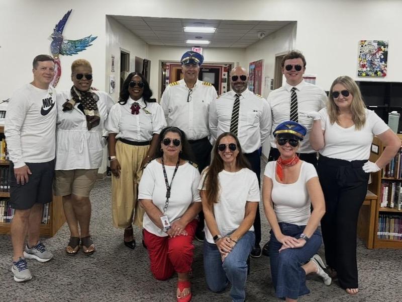 A group of people in a library, dressed in white shirts and sunglasses, posing together.
