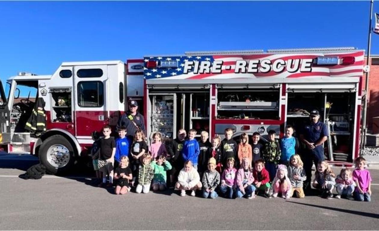 Children and firefighters pose in front of a fire truck with 'FIRE-RESCUE' written on it.