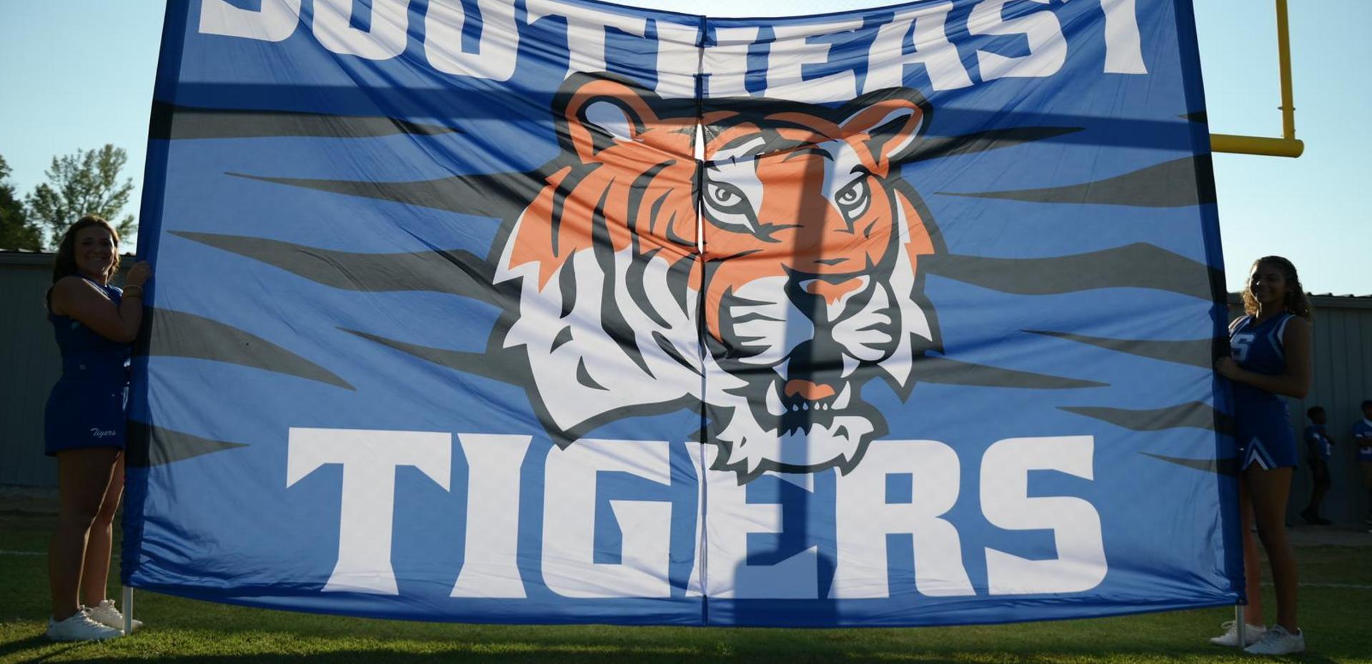 Cheerleaders holding a large banner featuring the Southeast Tigers mascot at a football game.