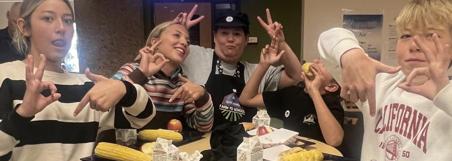 Group of students making fun hand signs while enjoying lunch at a table.