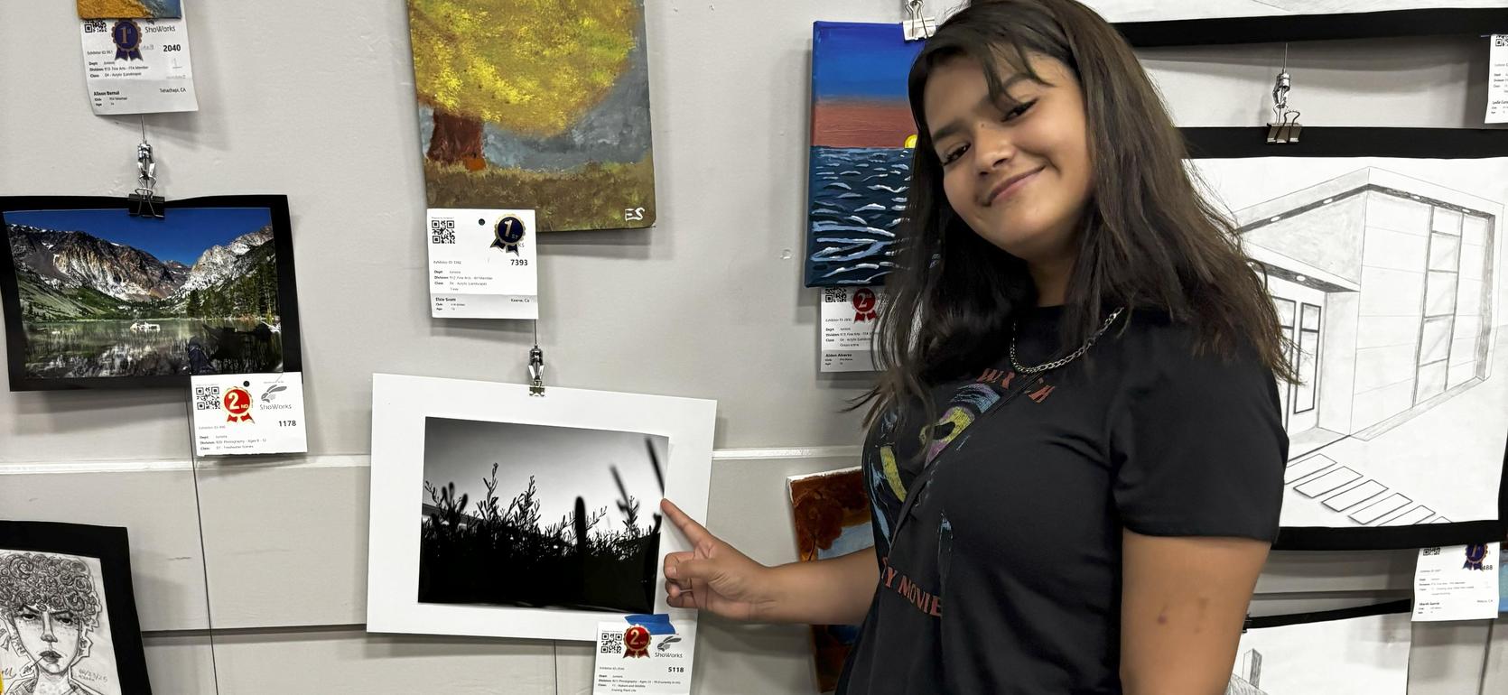 A person points at a black and white photograph of tall grass on a gallery wall.