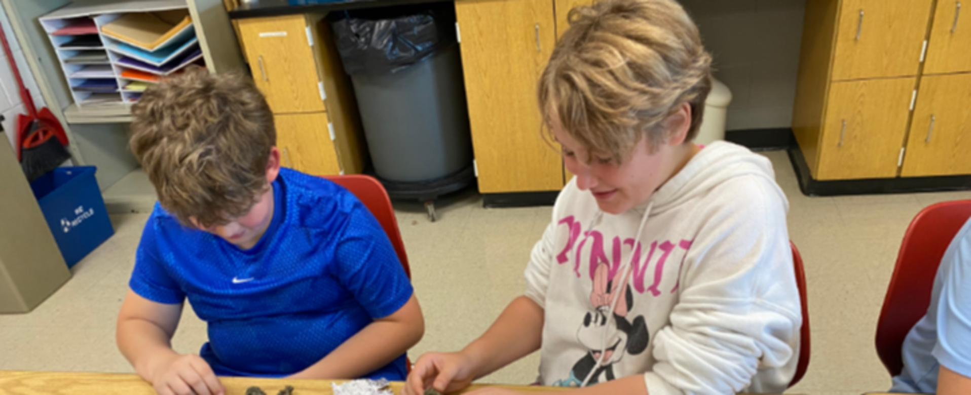 Two children engaged in crafting activities at a classroom table.