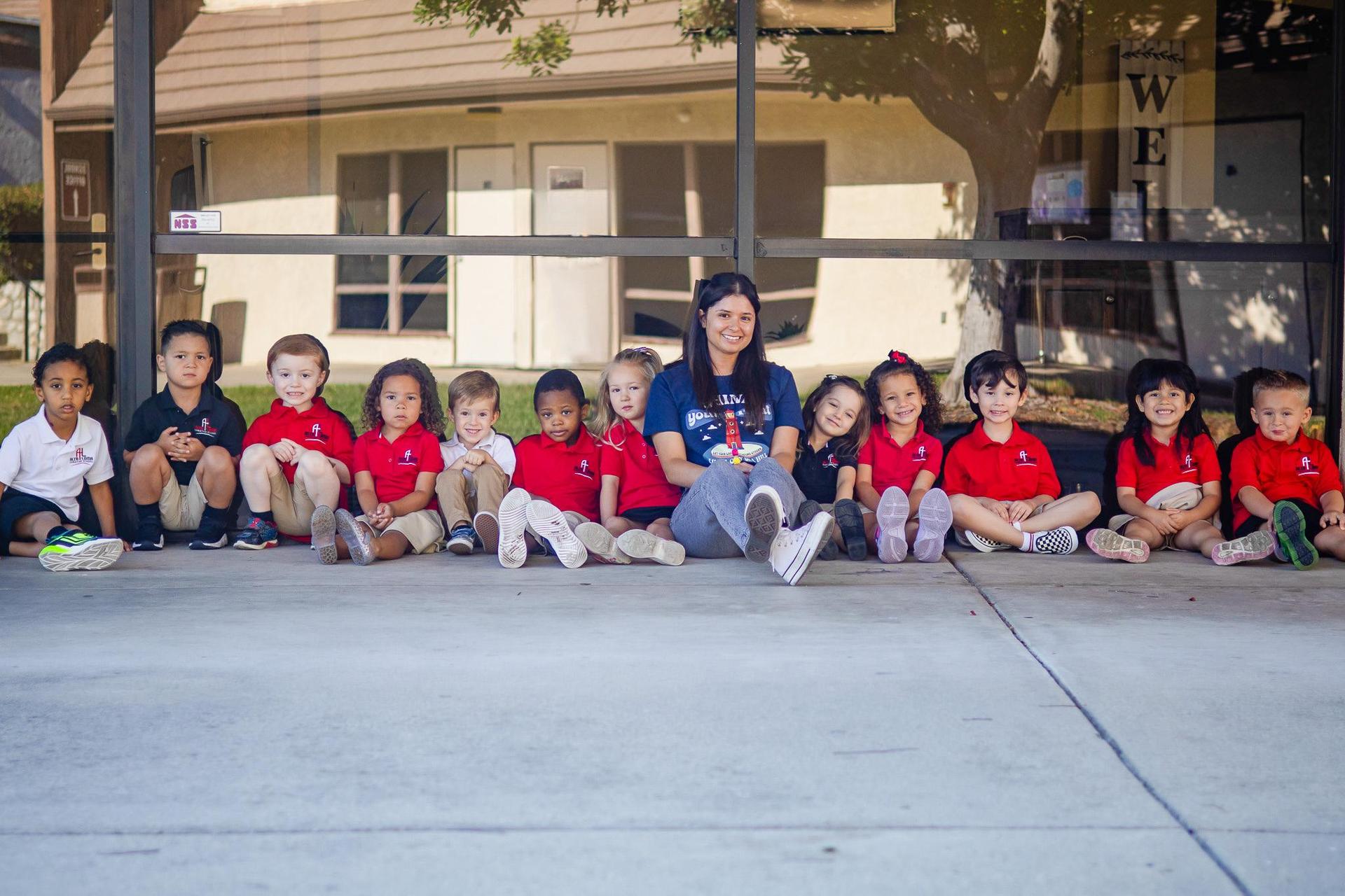 A preschool class sitting in a line outside.