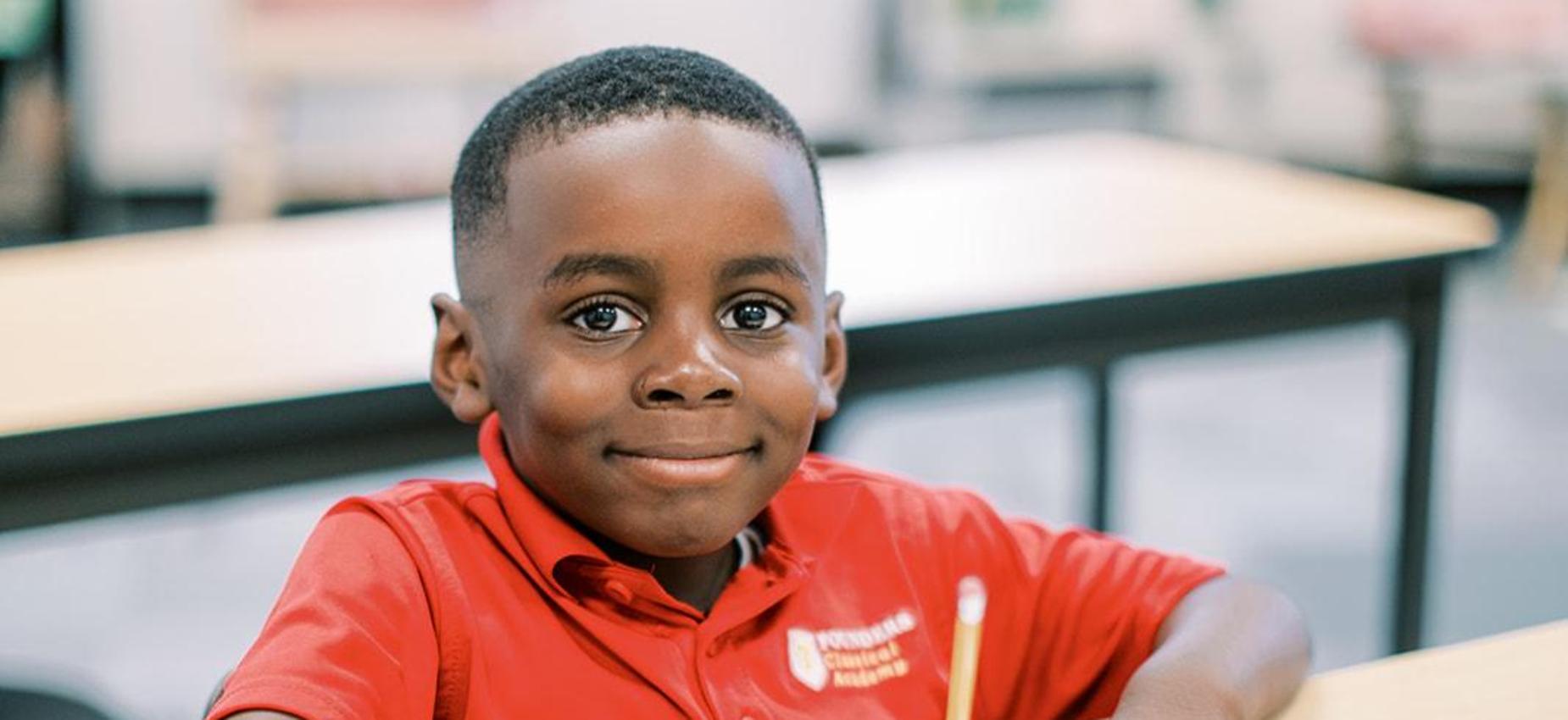 Smiling student in a red Founders polo writing at his desk