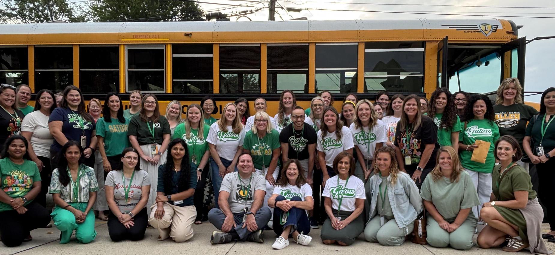 Group of teachers in green shirts posing in front of a yellow school bus.