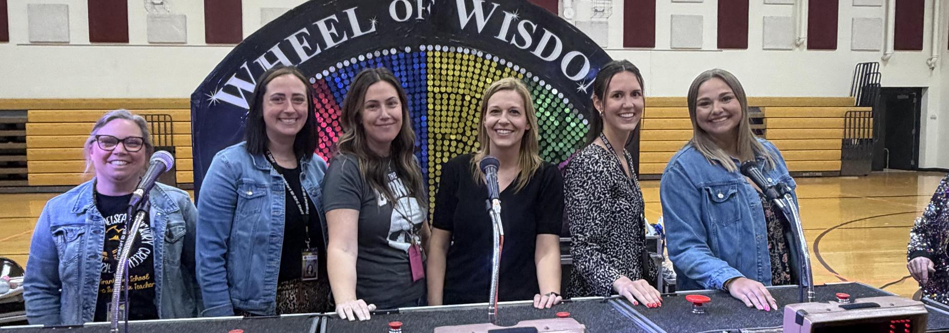 Group of six women standing in front of a colorful Wheel of Wisdom backdrop.
