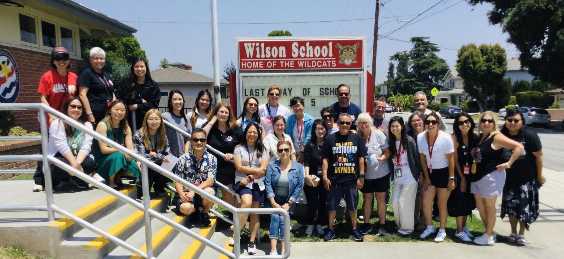 Group photo of staff and students in front of Wilson School sign, celebrating the last day of school.