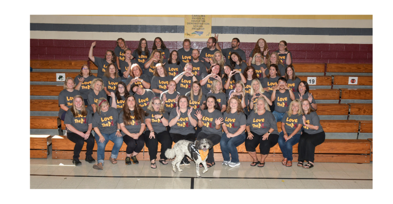 Group of people in matching shirts with a dog, posing on bleachers.
