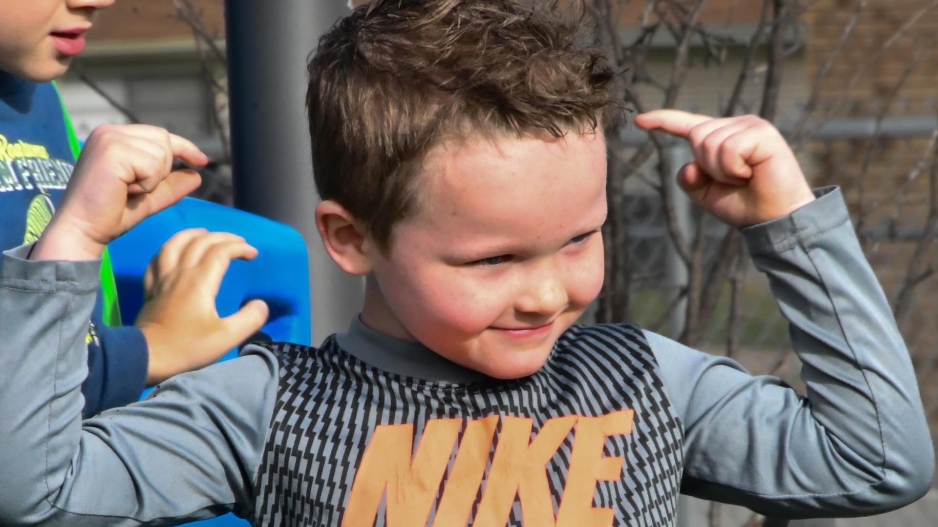 Boy smiling and flexing his muscles playfully while wearing sports attire.