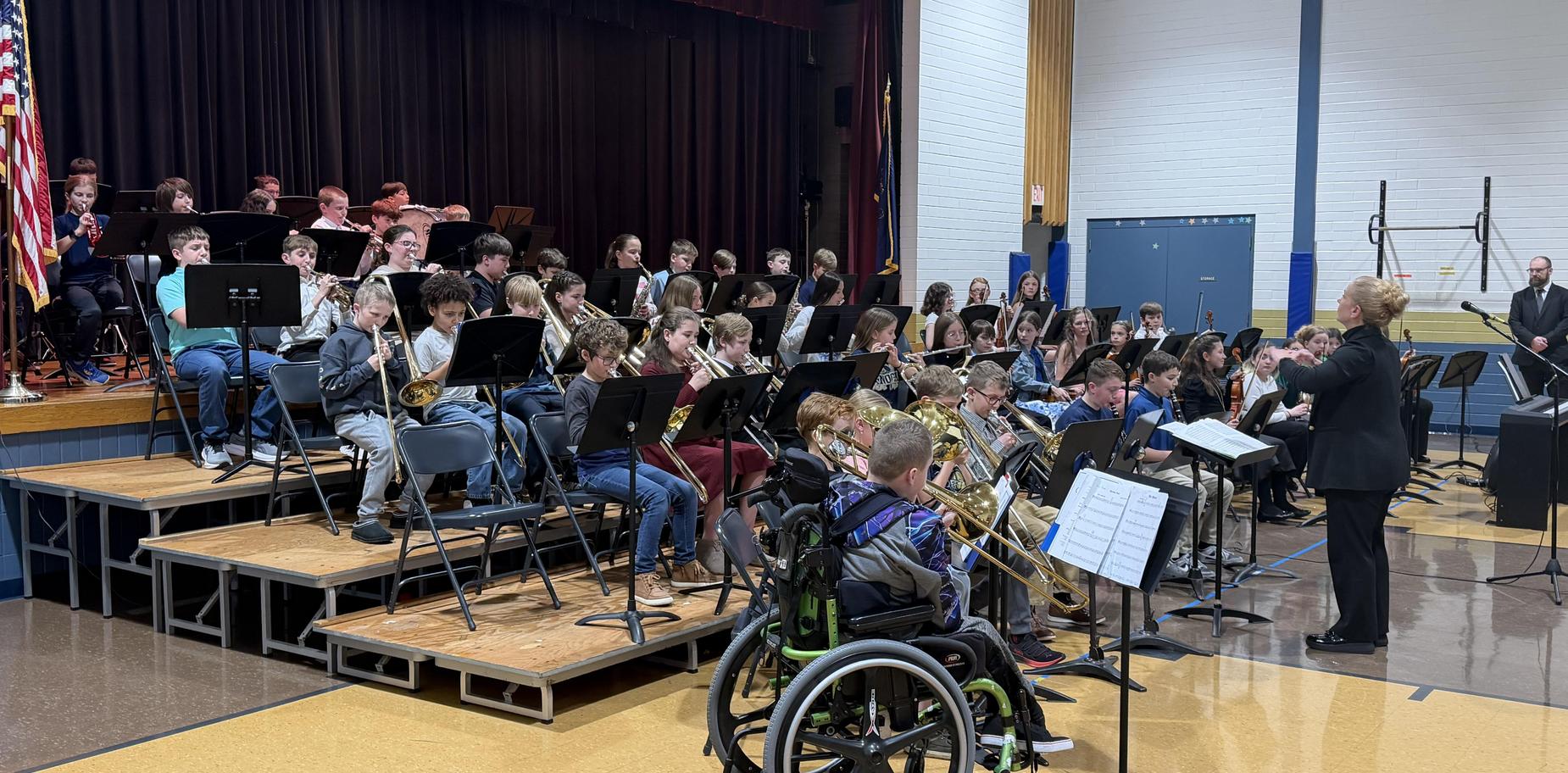 School band performing on stage with a conductor, featuring students in various instruments.