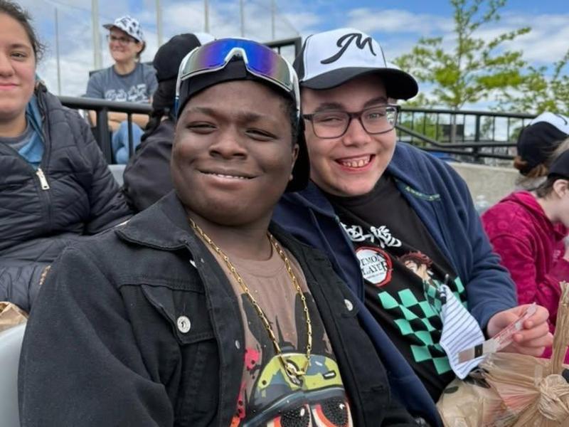 Two smiling boys sitting together, wearing sunglasses and casual clothing.