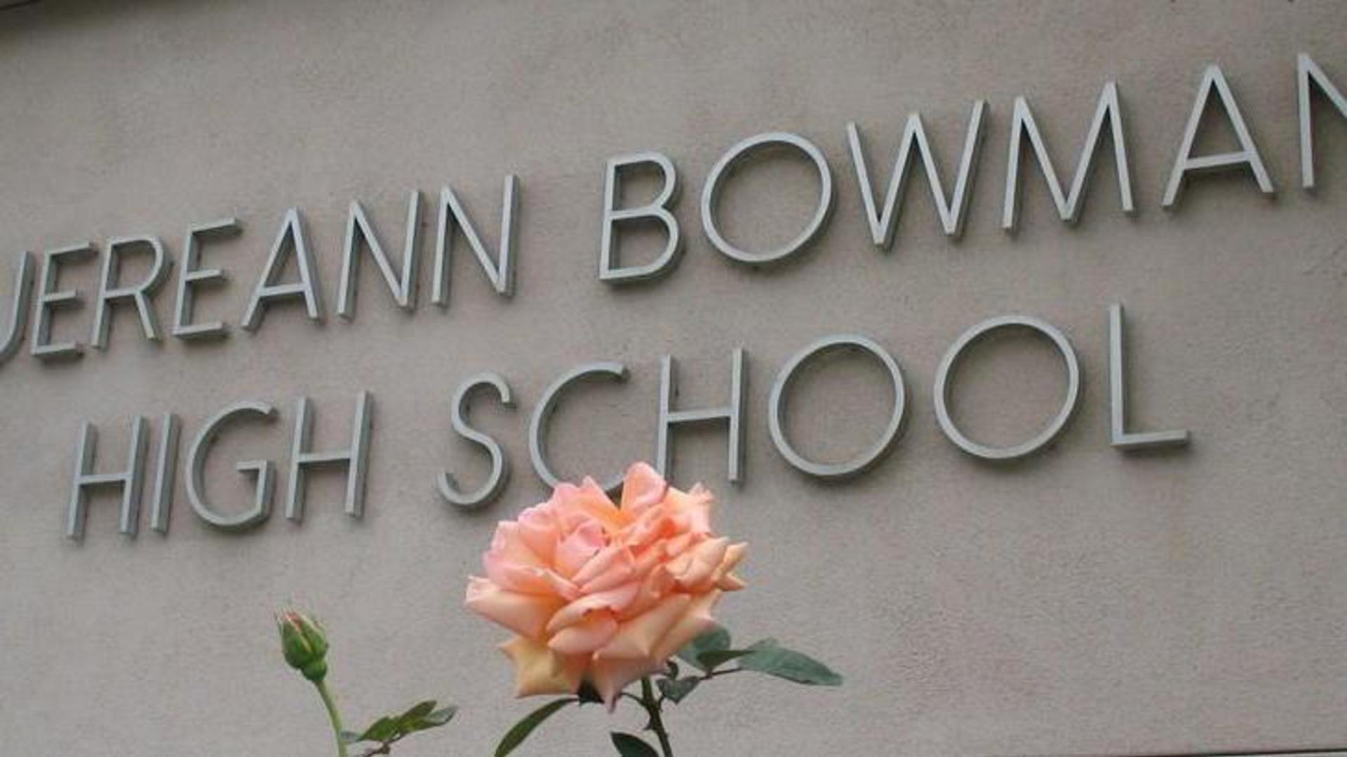 Close up of a peach colored rose blooming in front of the school sign that reads Jereann Bowman High School