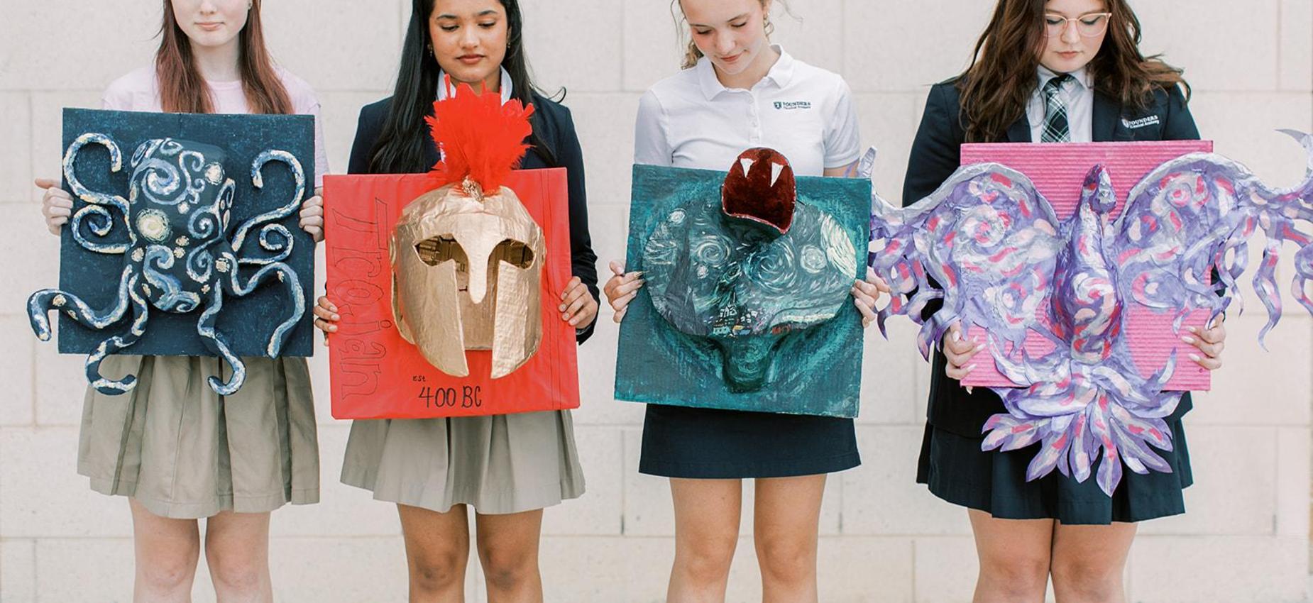 Four students hold up their artwork