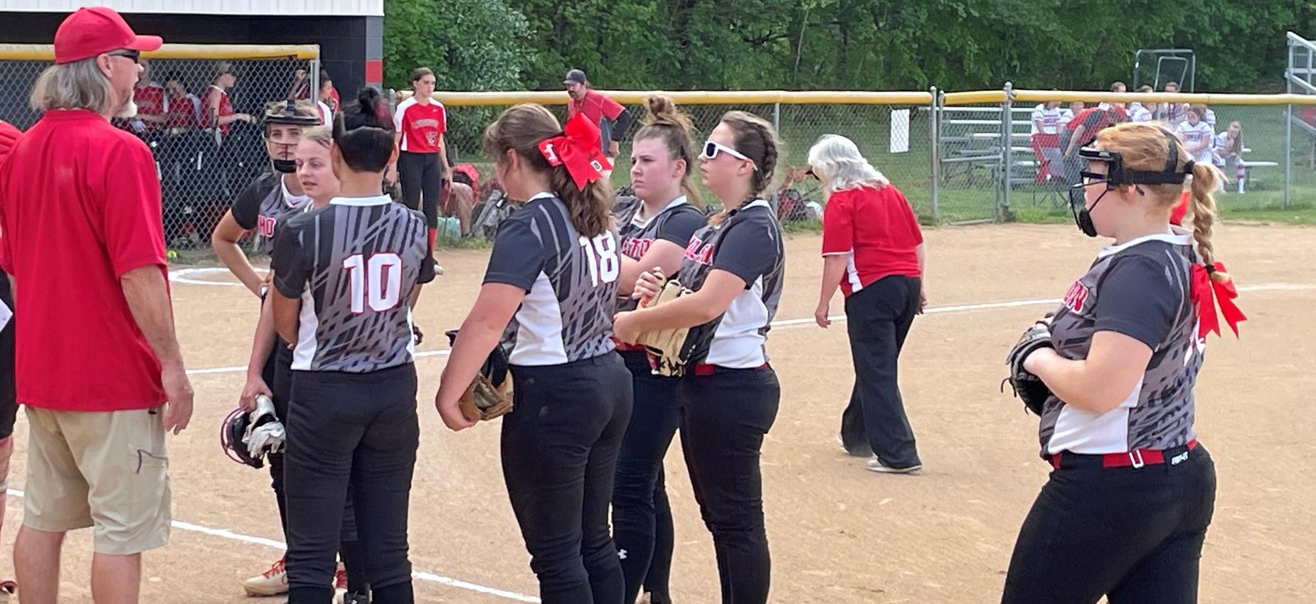 A group of softball players listen to a coach.
