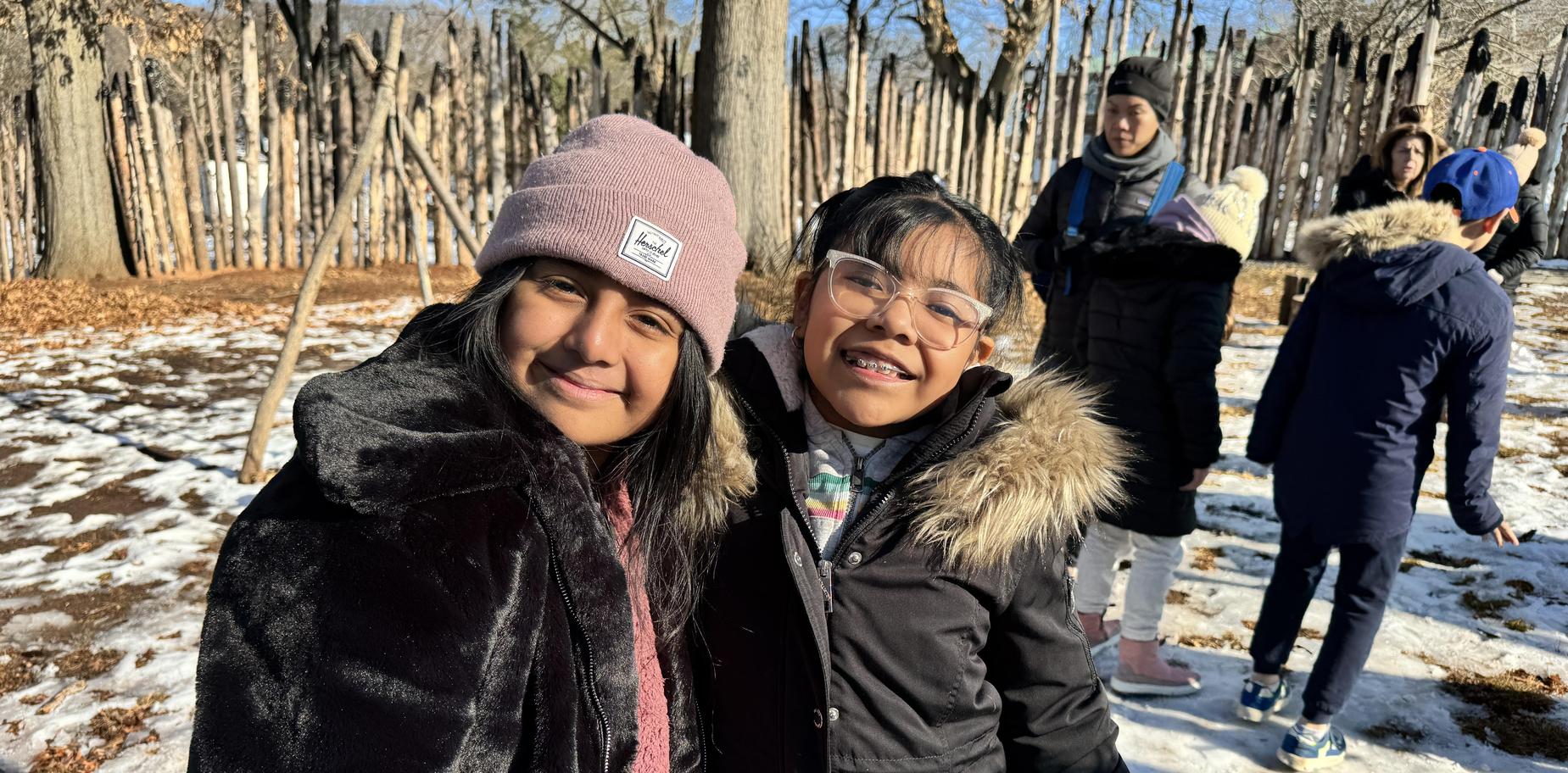 Two girls smiling and posing together in a snowy forest setting.
