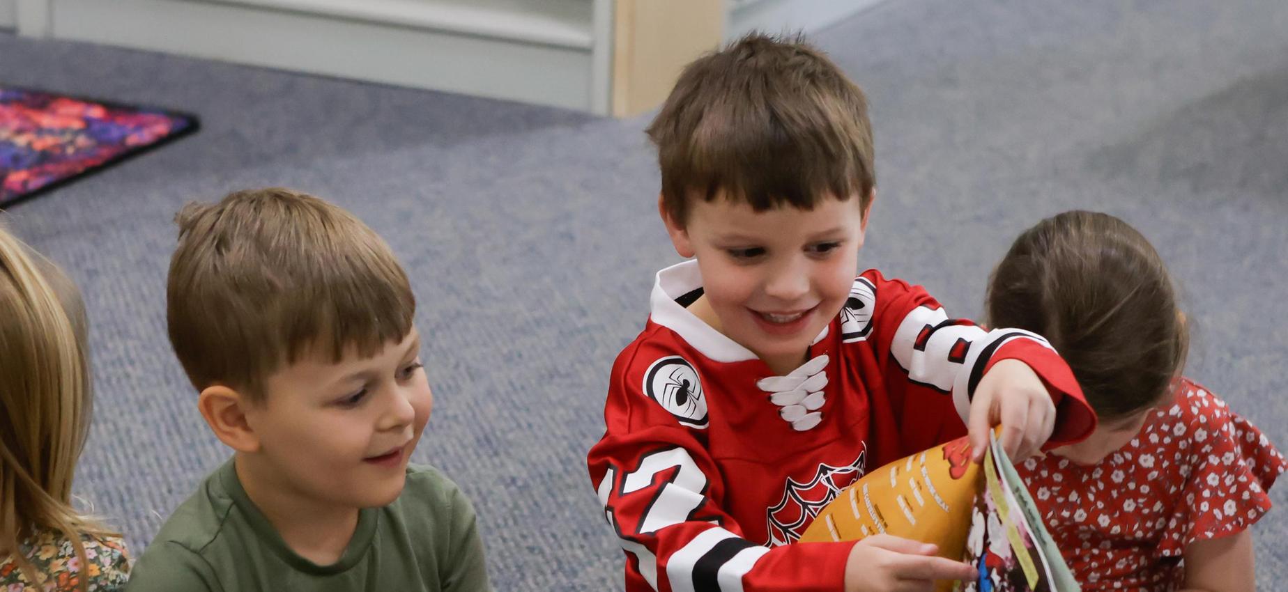 Children sitting in a classroom, one boy reading a book with excitement.