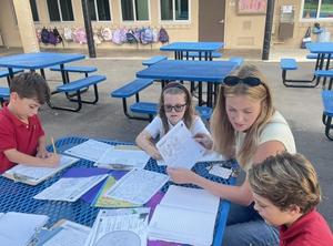 3rd grade teacher working outsdie with 3 students on narrative story
