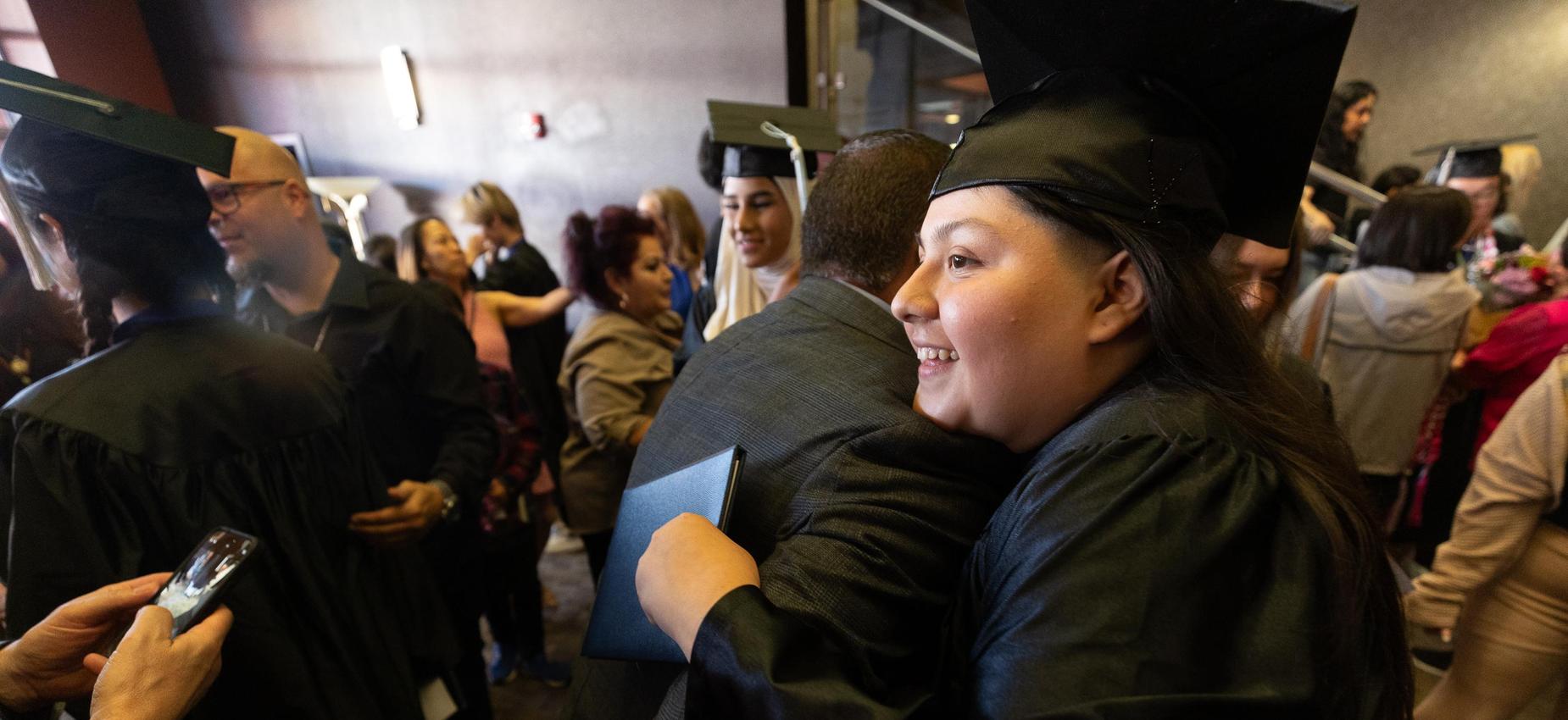 Graduates celebrate with hugs and smiles in a crowded venue.