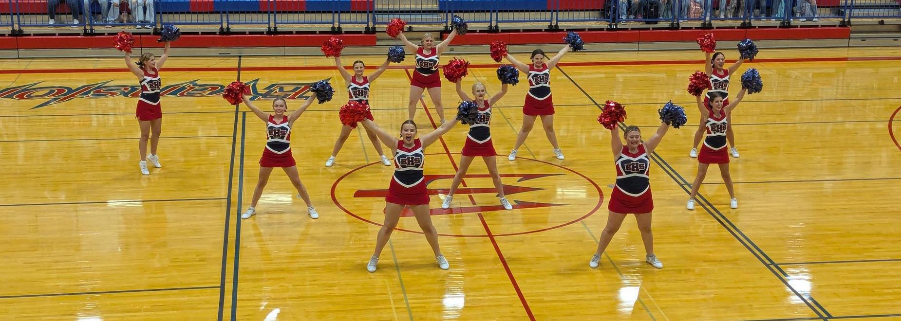 Cheerleaders displaying pom-poms in a dynamic formation on a gym floor.