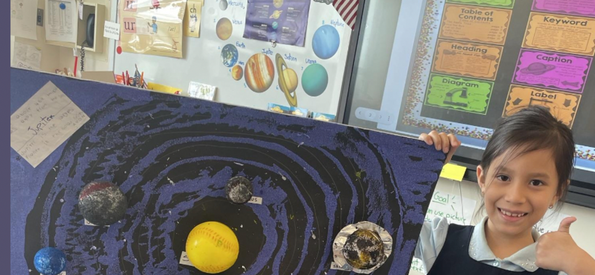 Child holding a handmade solar system model with labeled planets.