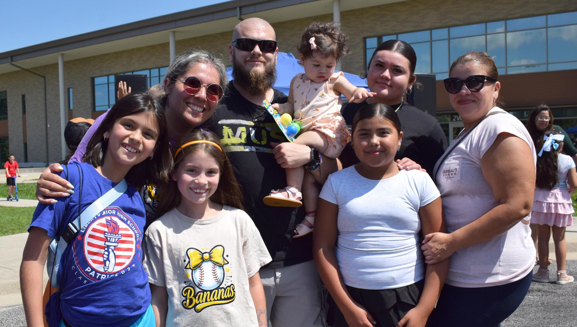 A diverse group of adults and children smiling together outside a school building.