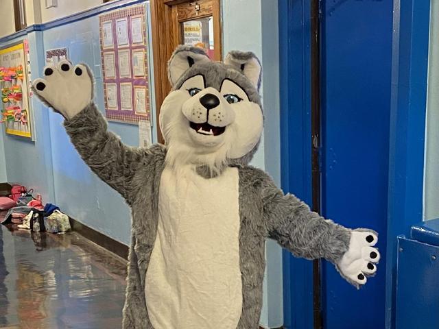 A person in a husky costume waving in a hallway.