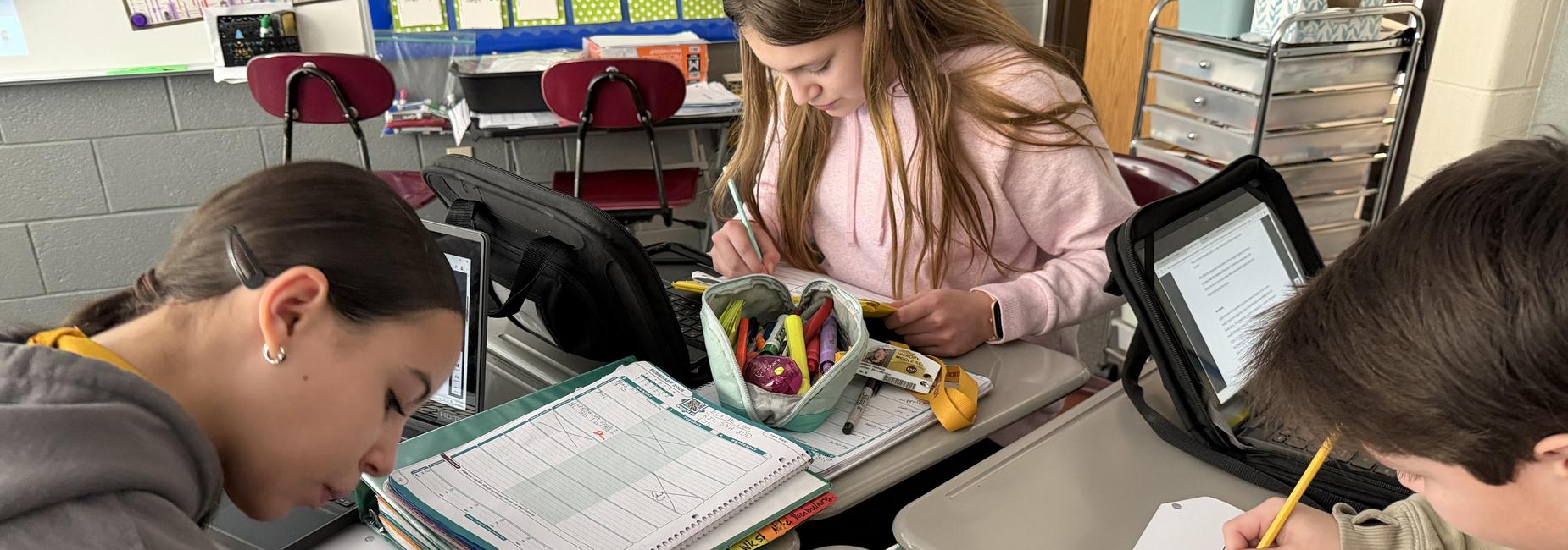 Three students working together at a school desk, focused on their assignments.