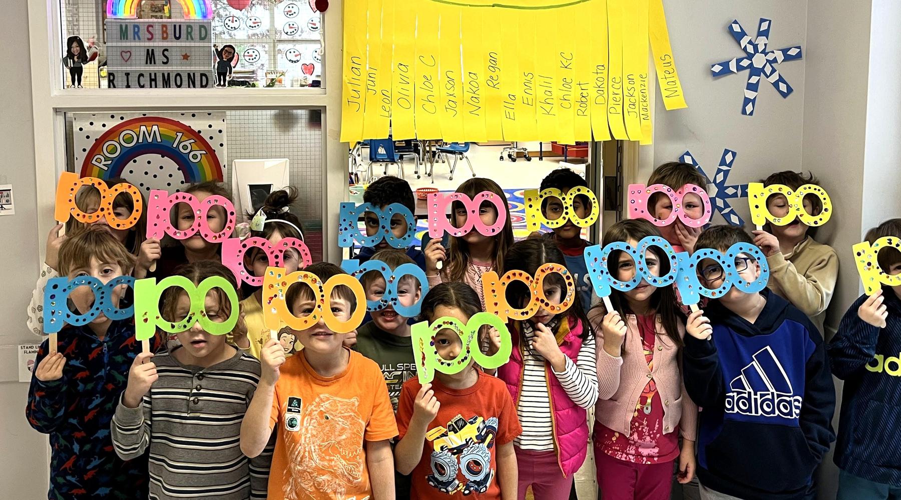 Students hold up colorful cutouts with letters, posing in a classroom.