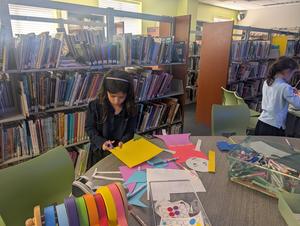 A girl cutting up paper for an invention in library.